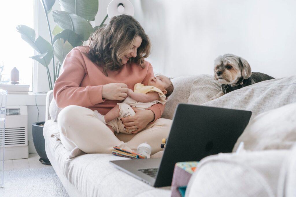 Mother holding a baby beside a laptop at home, illustrating workplace lactation and caregiving rights
