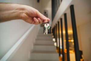 A hand holding house keys in a modern apartment hallway
