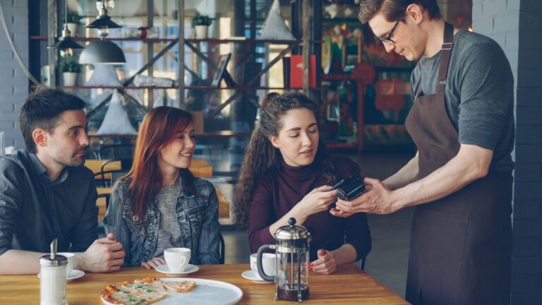 Restaurant customers paying a server by card at a cafe table