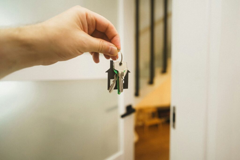A hand holding apartment keys near an open door, representing a tenant move-out and security deposit return.