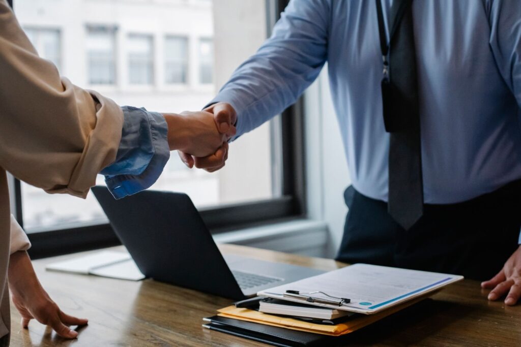 Two professionals shake hands over workplace documents and a laptop, representing employment rights and USERRA protections.