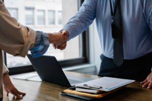 Two professionals shake hands over workplace documents and a laptop, representing employment rights and USERRA protections.