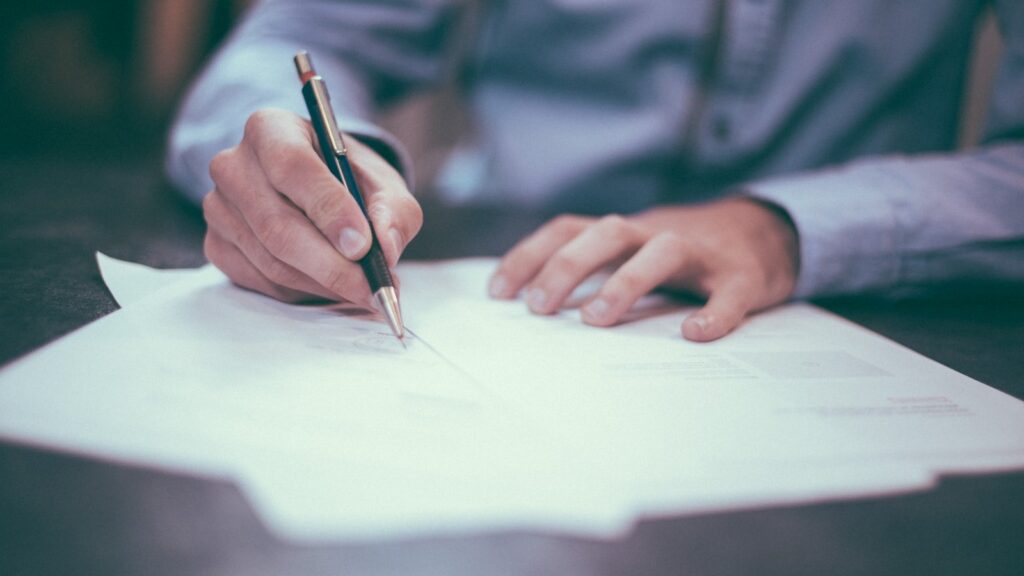 A person signing paperwork at a desk, representing a vendor contract dispute.