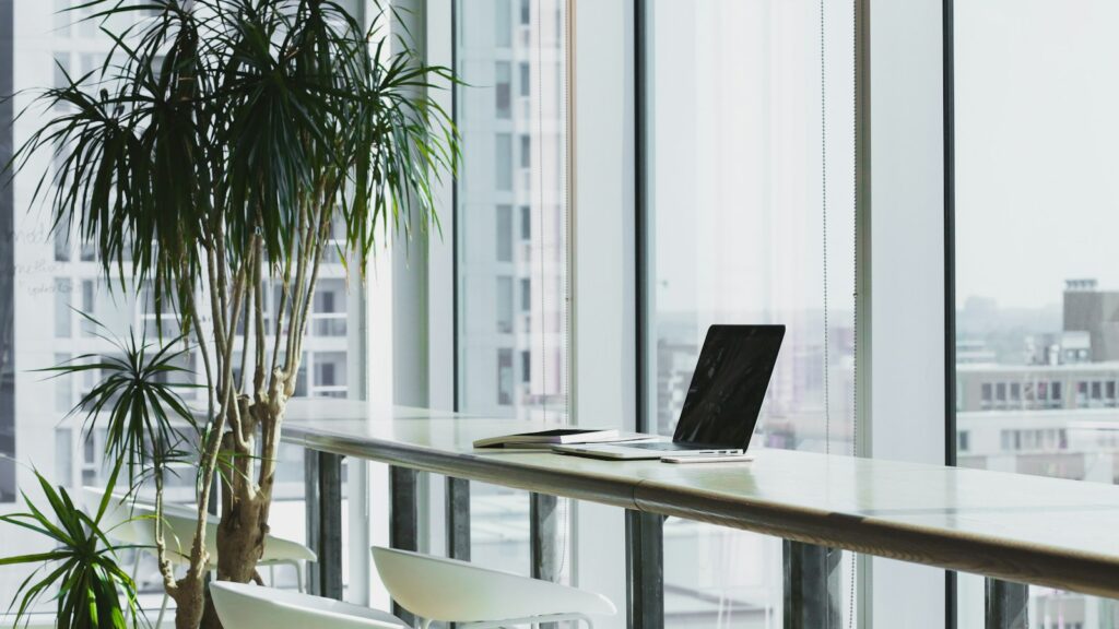 Office desk with a laptop beside large windows