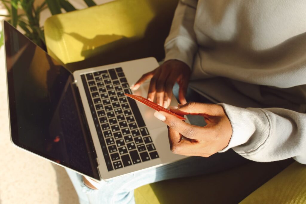 Person holding a payment card beside an open laptop